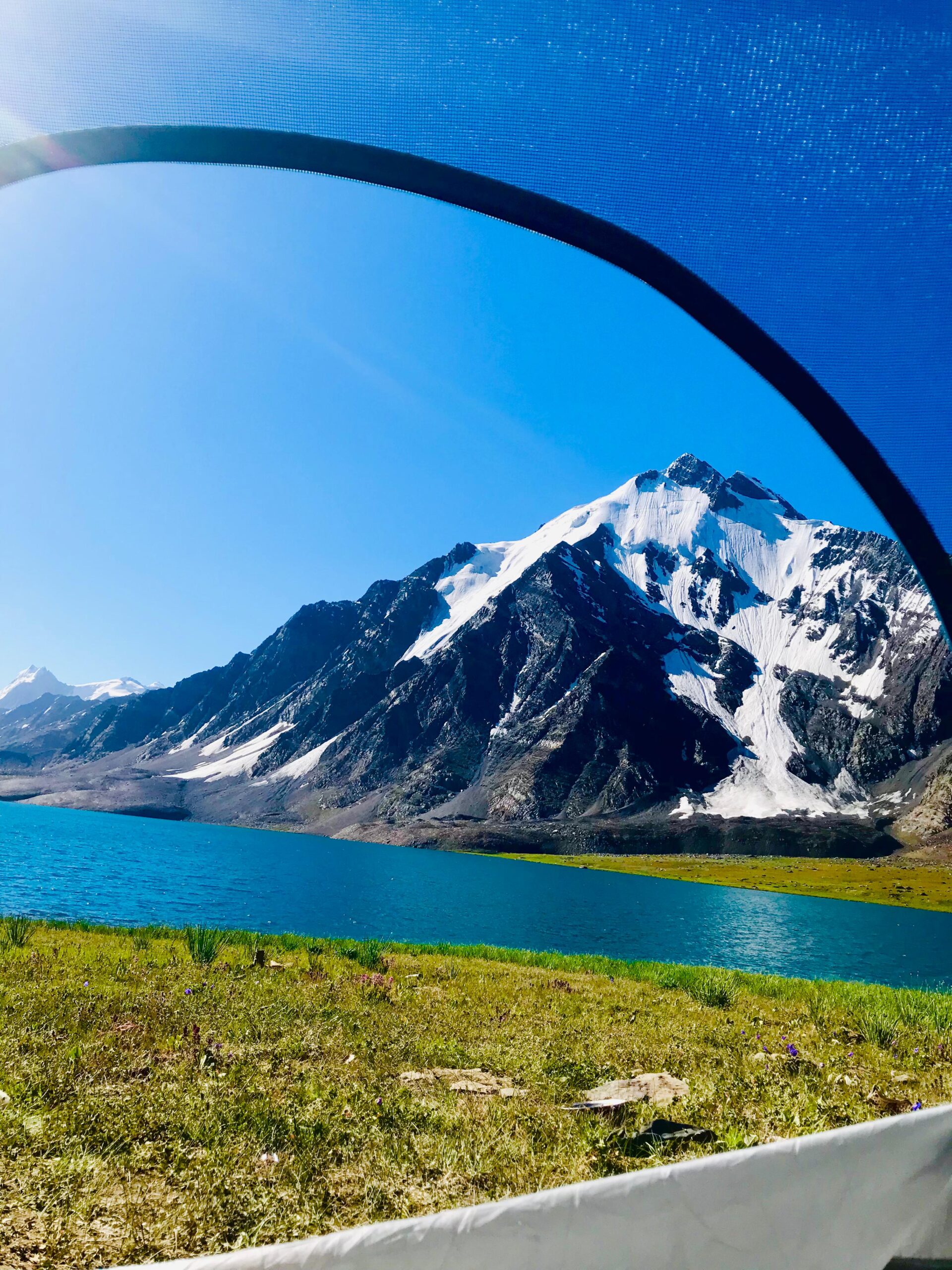 Colorful tents set up near Karambar Lake during sunset, surrounded by mountains and wildflowers. Karambar Lake Camping, Northern Pakistan Adventure, Trekking Campsites, Broghil Trek, Akmal Naveed Travel