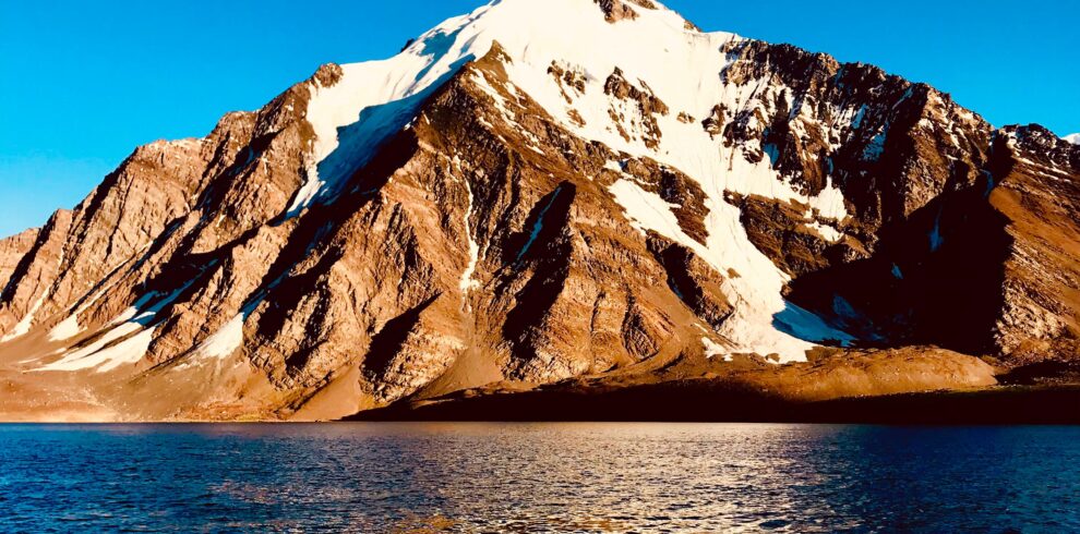 Still waters of Karambar Lake reflecting snow-covered mountain peaks under a pastel-colored sky.